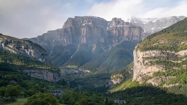 Sunlight and shadows moving across a green valley and rocky peaks in the pyrenees mountains