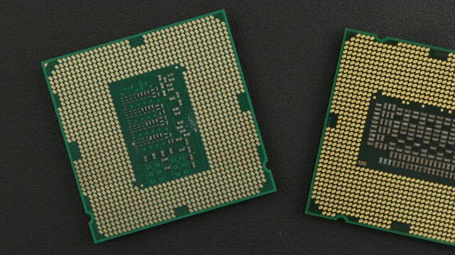 Two microprocessors with intricate gold contact pins rest on a dark surface. Ideal for technology presentations or educational materials on computer hardware.