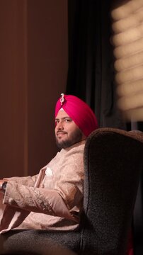Vertical Shot of Handsome Punjabi Groom In Traditional Sherwani And Pink Turban Relaxing Before Wedding