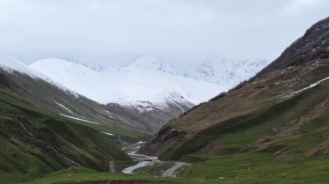 majestic snow covered Shkhara mountains and green valley with winding river, serene wilderness landscape for travel and adventure, Svaneti Georgia