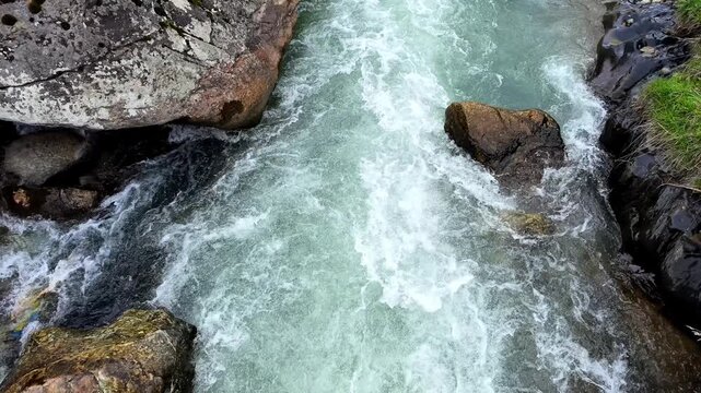 Top view of a rushing mountain stream with clear water flowing between textured grey rocks and stones, Mestia, Svaneti, Georgia