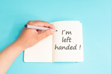 I am left handed is standing on notebook, writing with left hand, pen and table, lefty concept, handwriting a message