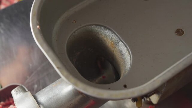 A person placing chunks of fresh beef into a running meat grinder during food preparation