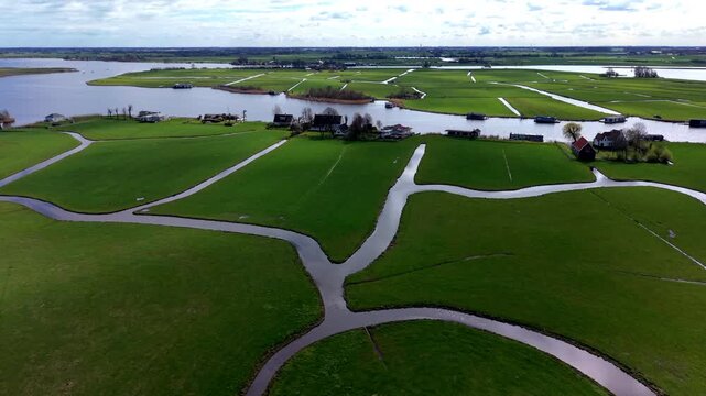 Aerial view of green rectangular fields divided by narrow water channels with scattered houses, farm buildings and distant lakes under partly cloudy sky in rural landscape