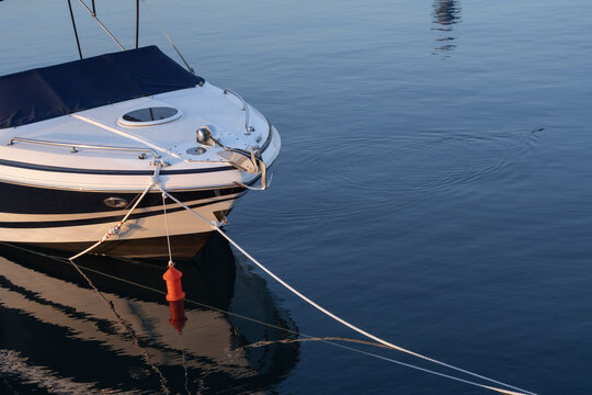 Bow of a moored motor yacht reflected in calm blue water at sunset in a Greek marina. Nautical travel, leisure boating and summer vacation concept with copy space.