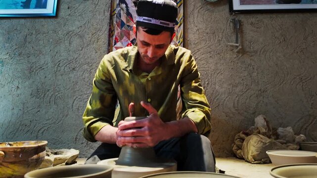 Smiling potter shaping clay vessel on wheel in traditional ethnic workshop