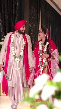 Vertical Shot of Happy Sikh Bride And Groom Walking Through Luxury Hotel Corridor With Foreground Flowers