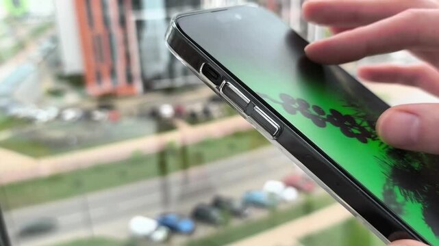Hand holds smartphone near a window in close up. Choosing and enlarging zooming photo content on screen with two fingers.
