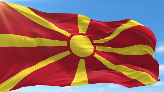 North macedonia national flag waving in medium close-up slow pan upward video against blue sky with clouds, vivid red field with golden sun of vergina radiating eight rays, dynamic silky fabric motion