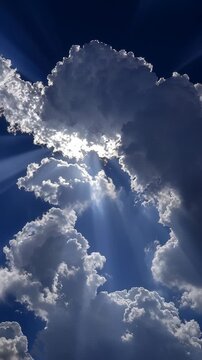 Dramatic sunlight beams shining through thick clouds in a deep blue sky.