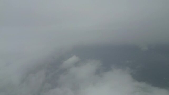 Aerial view of a cloudy sky from an airplane window, showing a gradual transition through layers of clouds and hints of blue sky peeking through the dense cloud cover