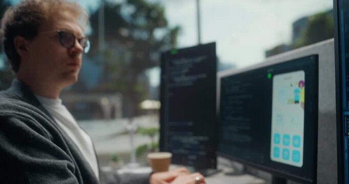 Portrait of Young Male App Developer Reviews Source Code and Checks a Mobile Interface Across Several Monitors, Working at Desk in Startup Office Building New Digital Products. Working Using Computer