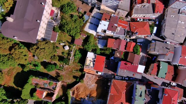 Top-down aerial drone view of European city rooftops and construction site. Drone shot of red tiled roofs, urban gardens, and an excavation site in Istanbul neighborhood during the day.