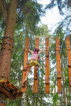 A girl climbs a curtain wall in an extreme sports park with safety gear.