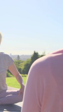 Vertical video: Friend cueing senior in grey tee doing bicycle legs for health on deck pink bottle