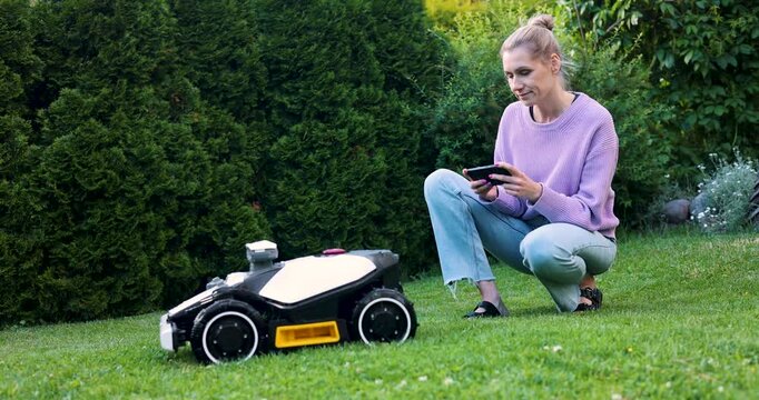 woman set up robotic lawn mower with smart phone at home garden