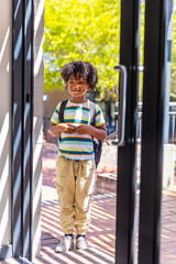 Naklejka premium African American child standing in glass doorway carrying dark backpack and wearing striped T-shirt