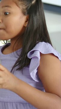 Vertical video: Raising glass, girl sipping orange juice in kitchen, placing glass down, scrunchie