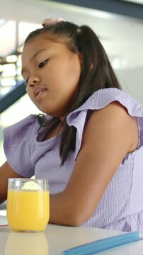 Vertical video: Looking at juice, girl in lilac top turning and picking pen near blue case at home