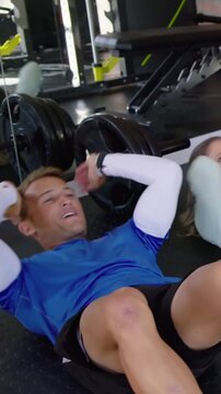 Vertical video: Starting, man in blue doing crunches training on mat near barbell, partner joining