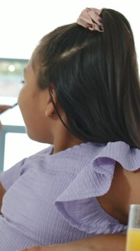 Vertical video: Hearing voice, girl at table turning, fixing hair tie, looking at juice, copy space