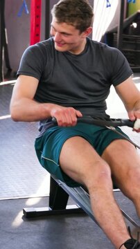 Vertical video: Strapping feet, man in shorts driving erg at gym training, adjusting taped grip