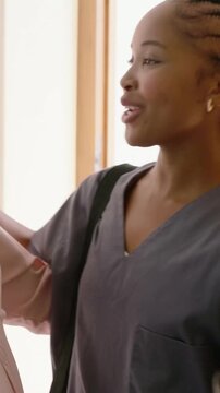 Vertical video: Approaching caregiver in gray scrubs smiling, greeting senior at door for home care