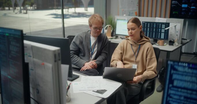Caucasian Male Developer and Female Engineer Discuss Code Together on a Laptop in a Modern Tech Office, Discussing Mobile Ecommerce App Logic, AI Features, Cybersecurity and Ux Design