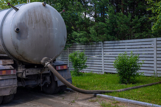 Vacuum truck pumping wastewater through flexible suction hose near backyard fence. Concept: wastewater management 