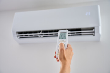 Hand changes air conditioner temperature with a remote control, setting the wall unit to 23...