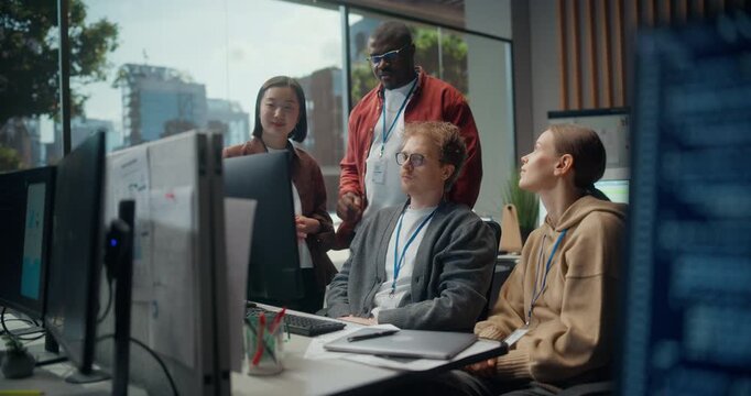 Seated Male Developer Points at a Screen, Briefing a Standing Asian Woman Engineer, Black Male Coder and Female Colleague on App Cybersecurity, AI Use and UI Design in a Modern Office Tech Meeting.