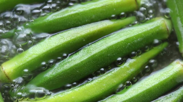 Boiling fresh okra pods in hot bubbling water inside a pot. Top view shot