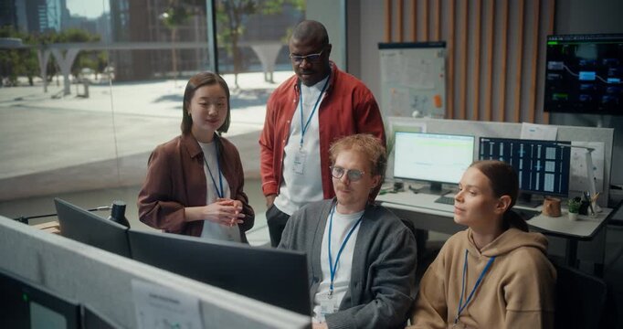 Software Dev Team Meeting in Modern Office: Seated Engineer Explains App Code as a Female Colleague Points at the Screen, While Standing Leads Weigh Cybersecurity, AI Algorithm and UI Design
