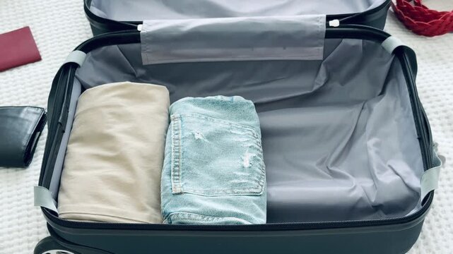 Folding beige shirt and packing it into a suitcase along with jeans and other clothing items