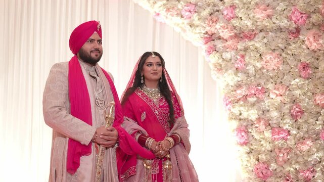 Traditional Sikh Bride and Groom Standing on Reception Stage with Floral Background
