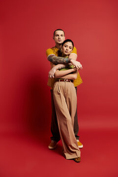 Young couple poses together in trendy outfits, showcasing affection in a striking studio.