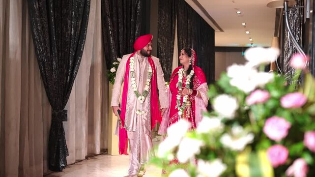 Happy Sikh Bride And Groom Walking Through Luxury Hotel Corridor With Foreground Flowers