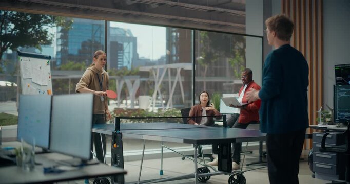 Two Software Developers Play Match of Table Tennis in Startup Office While Seated Colleagues Holding Laptop discuss App Code, Cybersecurity Logic and Ux Blending Teamwork With Playful Break.