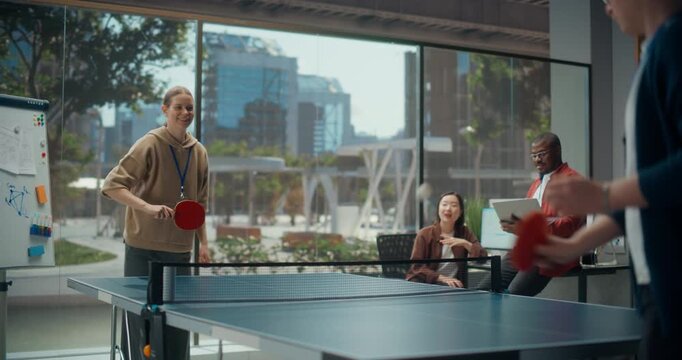 White Woman Programmer Play Table Tennis Ping Pong Match with Colleague Developer While Black Male Engineer and Asian Woman Designer watch the Game and Enjoy Having Fun.