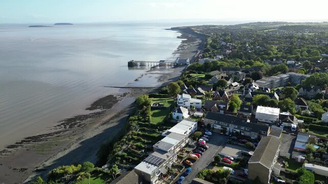 4K Aerial Drone Shot of Coastal Town with Pier Extending into Calm Sea, Sandy Beach, and Waterfront Houses Under Clear Sky, Penarth Pier, Cardiff, Wales, United Kingdom