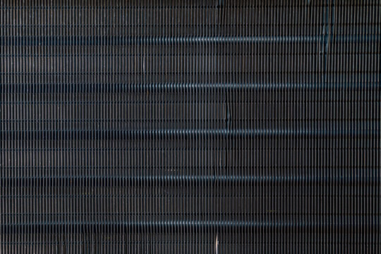 Close up texture of dark metal radiator fins background. Detailed abstract pattern of aluminum cooling coil grid, perfect for industrial, hvac engineering and mechanical background concept.