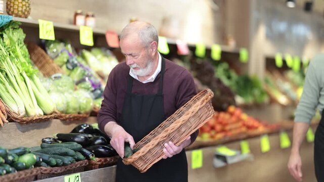 Mature seller working in supermarket and lays out fresh cucumber on counter. High quality 4k footage