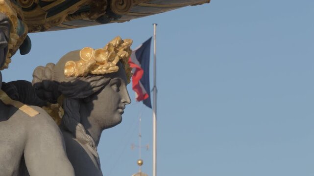 Static slow motion close up of an allegorical figure on the Fontaine des Mers at Place de la Concorde in Paris, with the French tricolor waving softly against a clear sky.