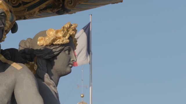 Static slow motion shot of a gilded allegorical statue on Fontaine des Mers at Place de la Concorde in Paris, with the French flag waving behind it.