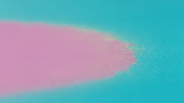 Spreading pink blotch rightward after dye drop in studio, forming pale yellow halo on cyan field