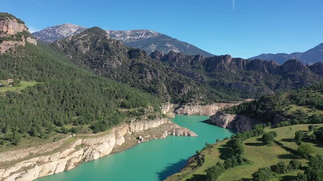 Scenic view of Llosa del Cavall reservoir, with turquoise waters, formed by dam on Cardener River in Spanish province of Lleida, framed by rocky Busa mountain range and lush greenery in summer