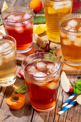 Summer refreshing drink, non alcohol tea based cocktails, iced tea varieties in different glasses, with fruit juices - strawberry, peach, apricot, cherry cold tea on wooden cozy background © ricka_kinamoto