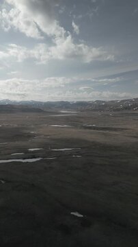Vertical aerial shot of drone flying forward over spring mountain steppe valley against snowy peaks. Smartphone 916 aspect ratio. RAW flat profile uncorrected video footage.