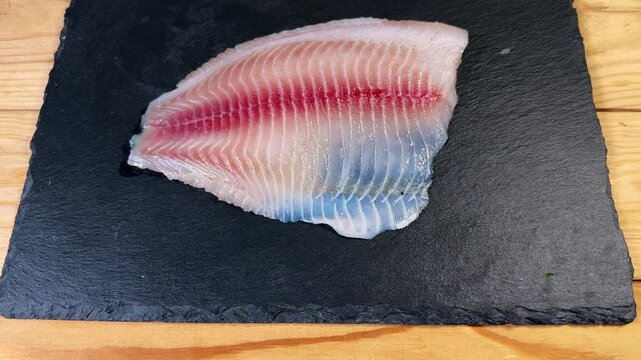 Raw defrosted tilapia filet on black flat slate plate