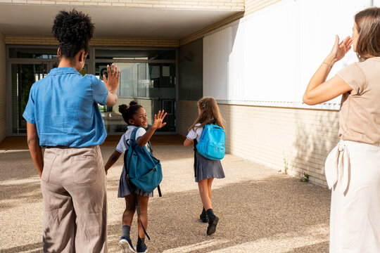 Parents waving goodbye to students entering school building